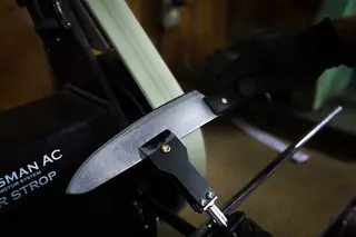 Knife positioned against a sharpening belt in a workshop