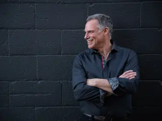 Portrait of a person smiling with folded arms against a dark brick wall