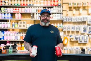 Person holding two cans in front of colourful product shelves