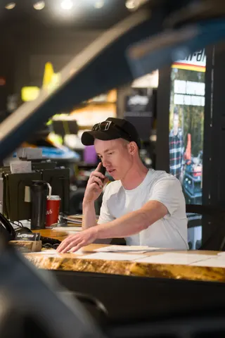 Person seated at a wooden counter beside shop refrigerators