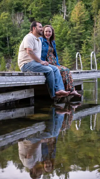 Couple sitting on a wooden dock with their reflections in the water