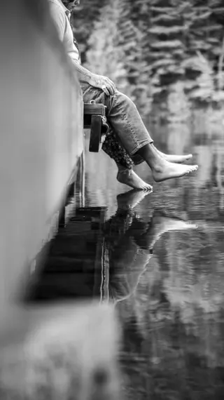 Black-and-white detail of bare feet and reflections beside a dock