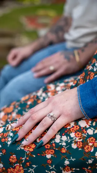 Engagement ring on a hand resting against a floral dress