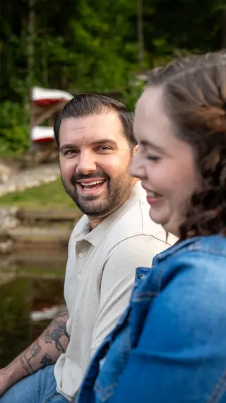 Couple smiling at one another beside a wooded lake