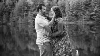 Black-and-white view of a couple facing one another by a lake