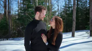 Couple smiling at one another among snow-covered trees