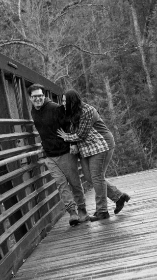 Black-and-white portrait of a couple laughing on a wooden bridge