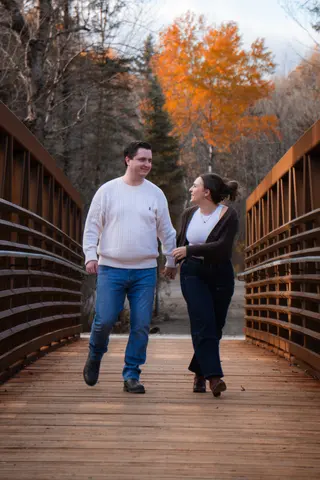 Couple holding hands as they walk across a bridge in autumn