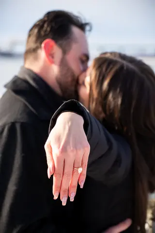 Couple kissing with an engagement ring held toward the camera