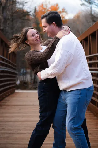 Couple smiling and turning together on an autumn footbridge