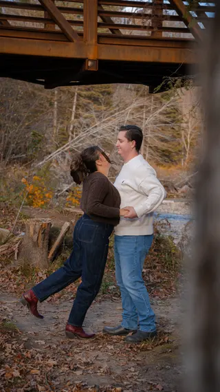 Couple facing one another below an autumn footbridge