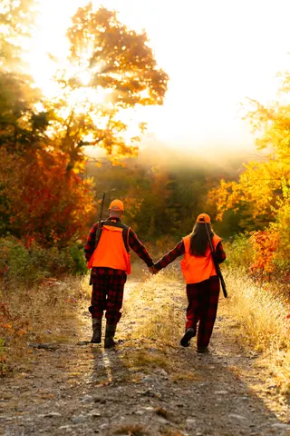 Couple walking hand in hand along an autumn trail in orange safety vests