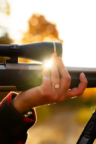 Engagement ring visible on a hand resting against a long gun