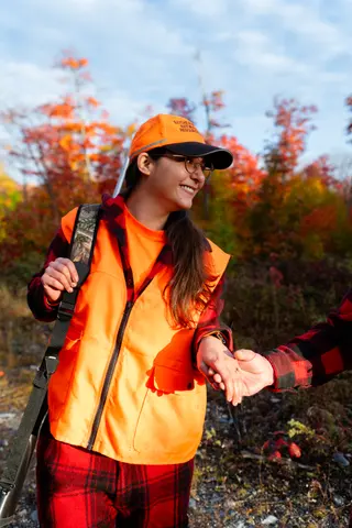 Person in an orange safety vest holding their partner’s hand on an autumn trail