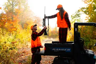 Couple posing with a long gun beside an off-road vehicle