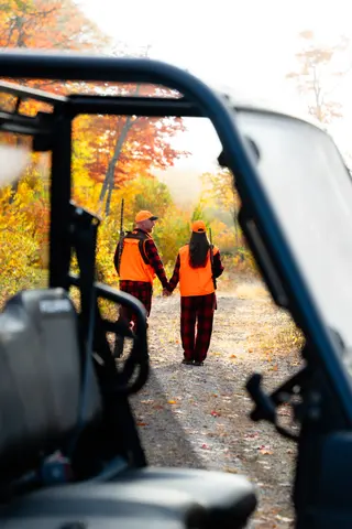 Couple walking through autumn trees, viewed past an off-road vehicle