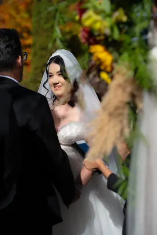 Bride smiling during an outdoor ceremony with autumn flowers behind her