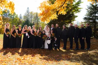 Wedding party gathered beneath trees with golden autumn leaves