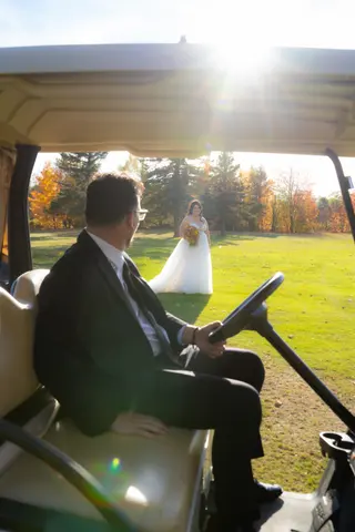 Groom looking toward the bride from a sunlit golf cart