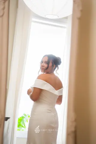 Bride looking back over her shoulder beside a sunlit window