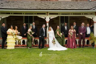 Wedding party gathered on a lawn in front of a covered porch