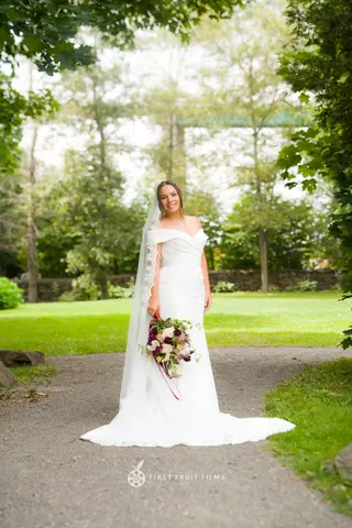 Bride holding a bouquet on a tree-lined garden path