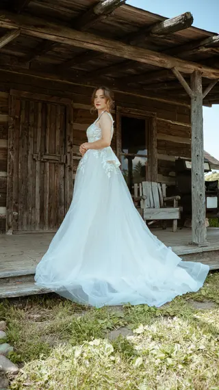 Bride standing beside a rustic wooden building with her dress train spread out