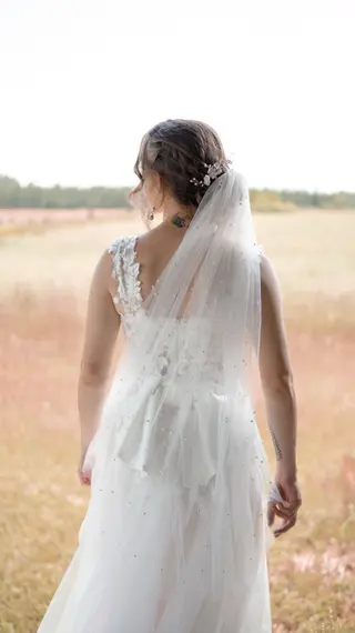 Bride’s veil and lace dress seen from behind beside a field