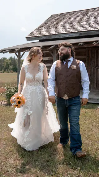 Bride and groom walking together past a rustic wooden building