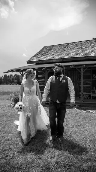 Black-and-white photograph of newlyweds walking across a lawn