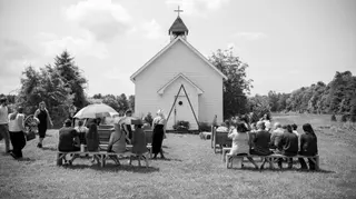 Black-and-white view of a wedding ceremony beside a small chapel