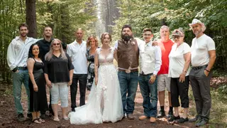 Wedding guests gathered with the couple on a forest path