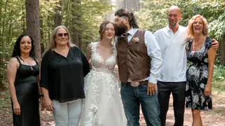 Newlyweds posing with guests among tall trees