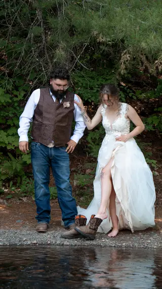 Bride lifting her dress beside the groom at the water’s edge