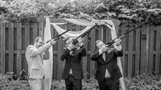 Black-and-white photograph of three suited wedding guests holding long guns