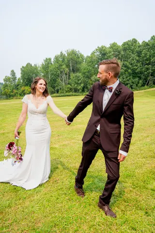 Bride and groom holding hands as they walk across a grassy field