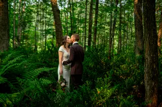Bride and groom kissing among green ferns and trees
