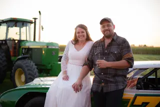 Bride and groom posing beside a tractor and a race car