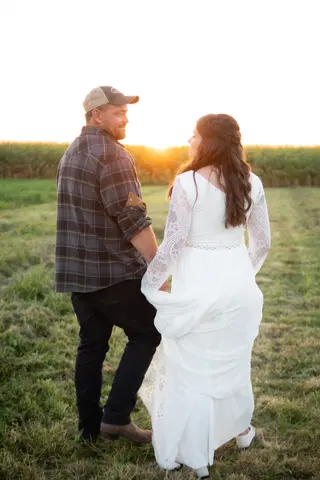 Newlyweds walking toward the evening sun in a field