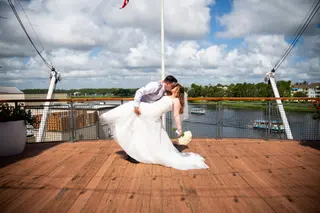 Newlyweds sharing a kiss on a waterfront deck under a cloudy sky