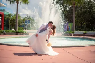 Groom dipping the bride beside a fountain and palm trees