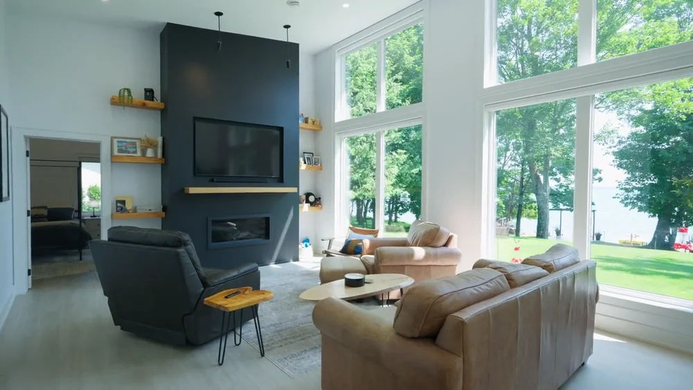 A bright living room with tall windows and a waterfront view in a First Fruit Films property tour